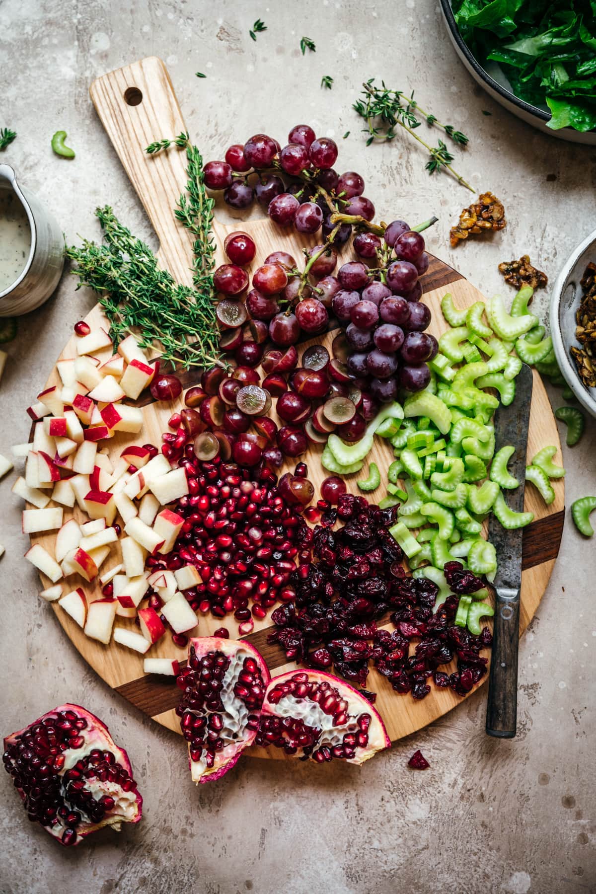 overhead view of ingredients for waldorf salad on a cutting board, including celery, grapes, dried cranberries, apples and pomegranate.