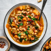 close up overhead view of vegan bean soup in a bowl on white linen surface.