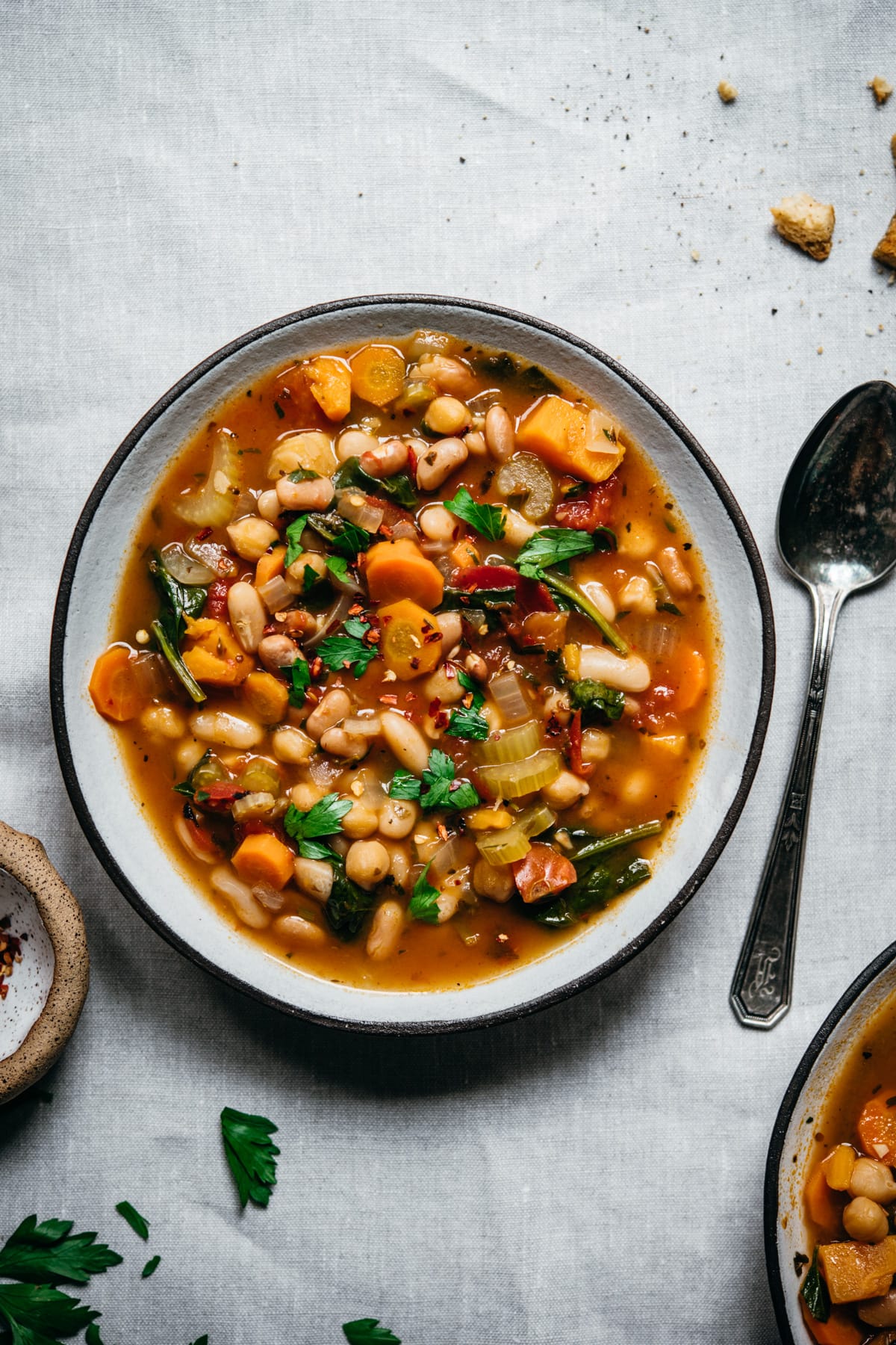 overhead view of vegan bean soup in a bowl on white linen surface. 