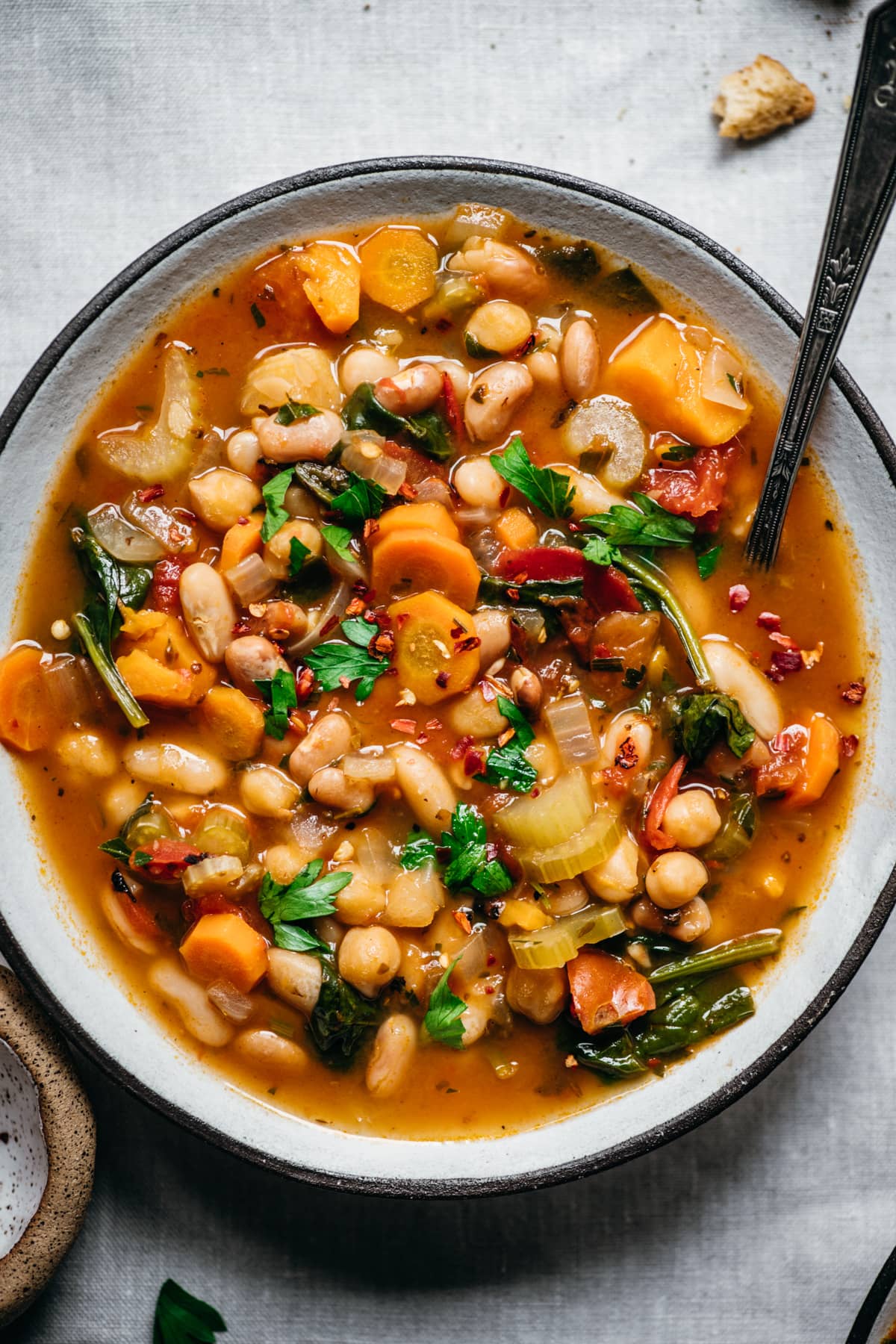 close up overhead view of vegan bean soup in a bowl on white linen surface. 