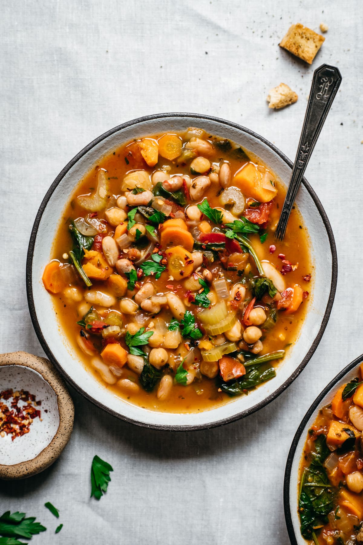 overhead view of vegan bean soup in a bowl on white linen surface. 