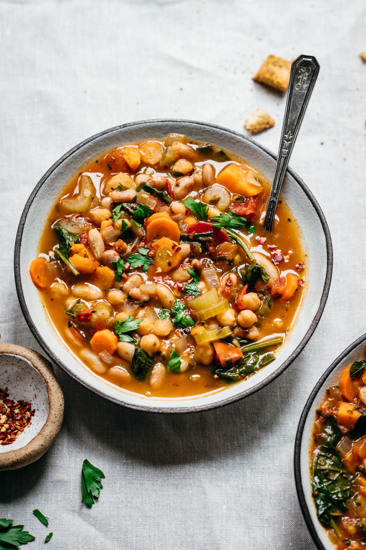 side view of vegan vegetable bean soup in white bowl on white linen. 