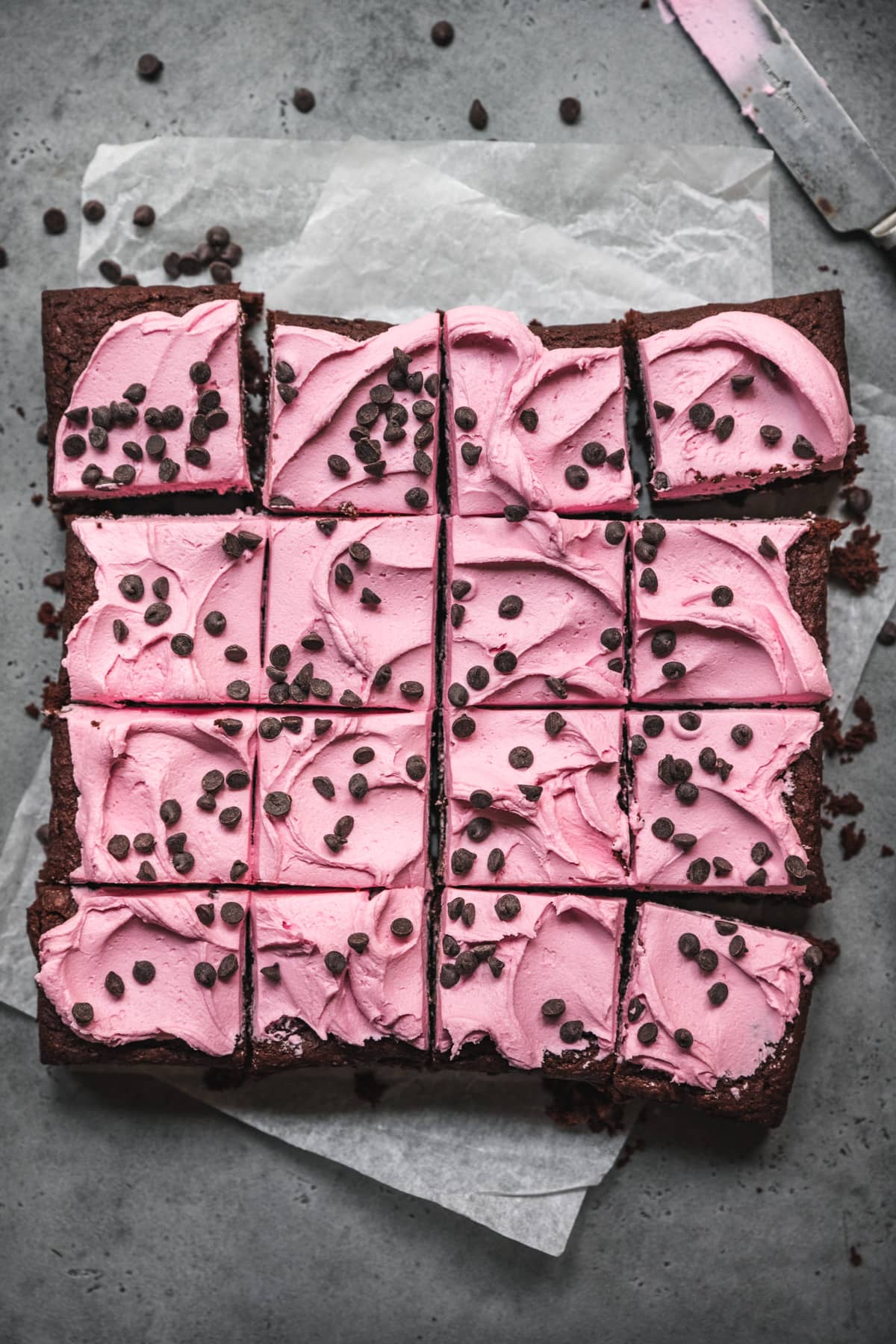 overhead view of beet brownies sliced and topped with pink frosting and chocolate chips. 