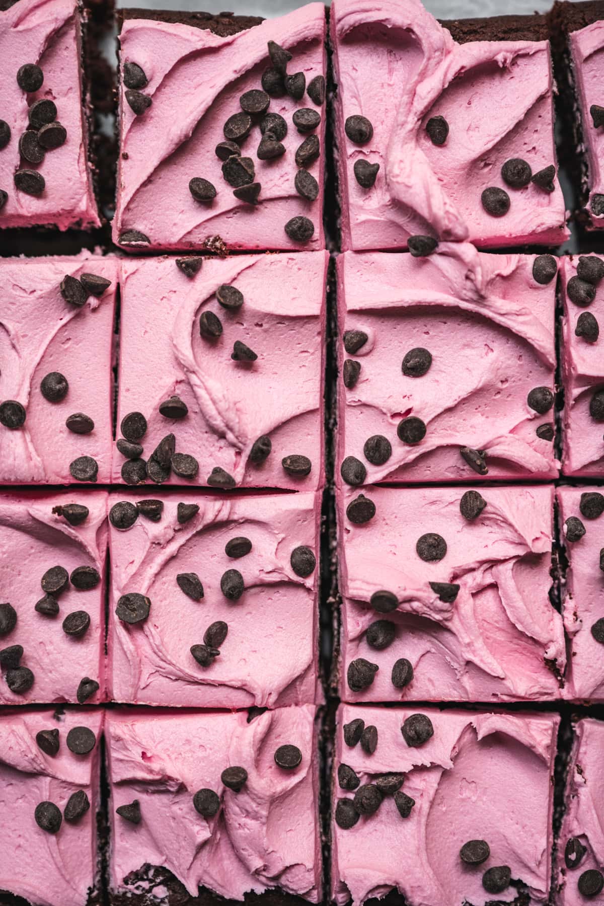 overhead view of beet brownies sliced and topped with pink frosting and chocolate chips.