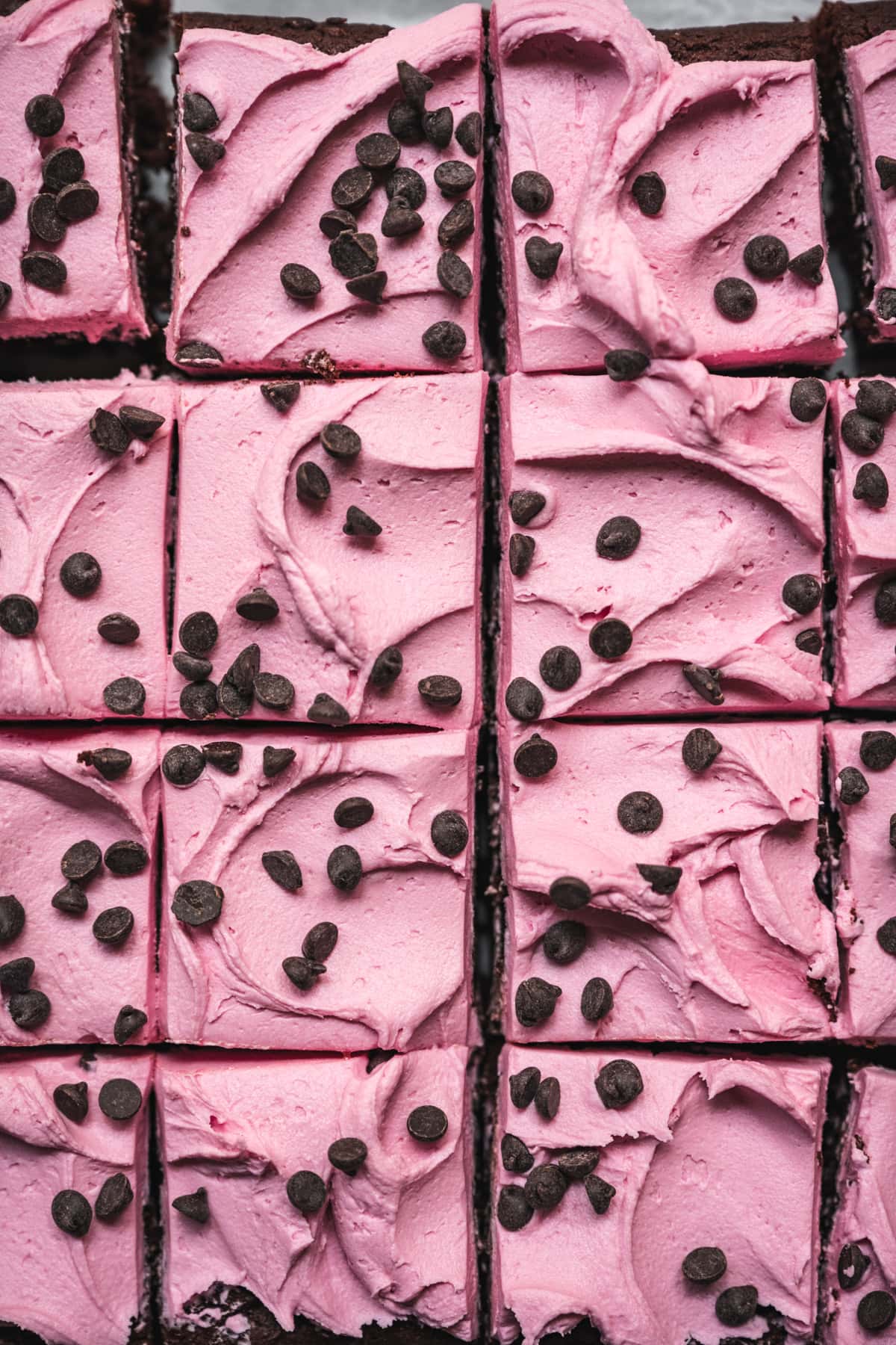 overhead view of beet brownies sliced and topped with pink frosting and chocolate chips. 