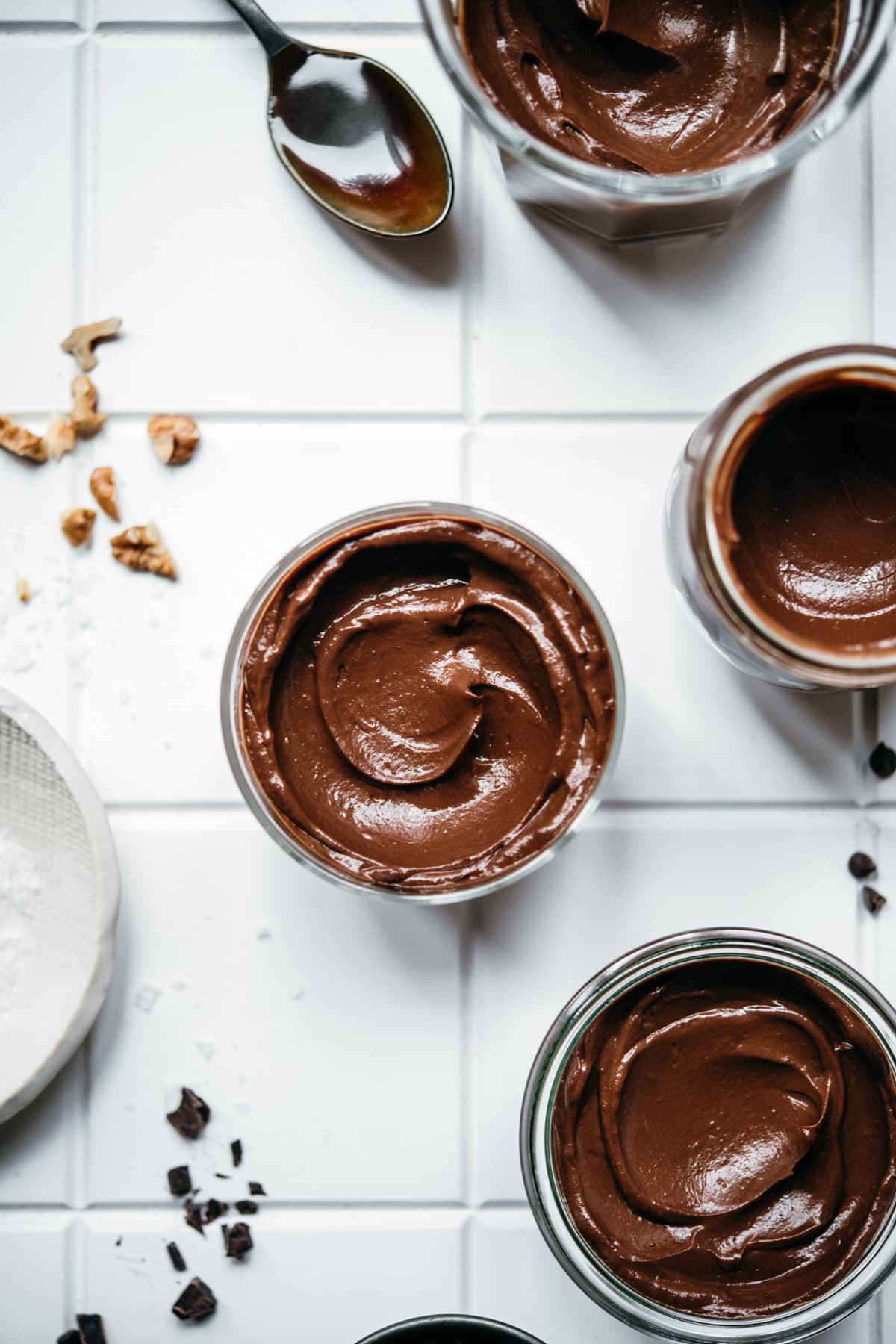 overhead view of jars of vegan avocado chocolate mousse on white tile. 