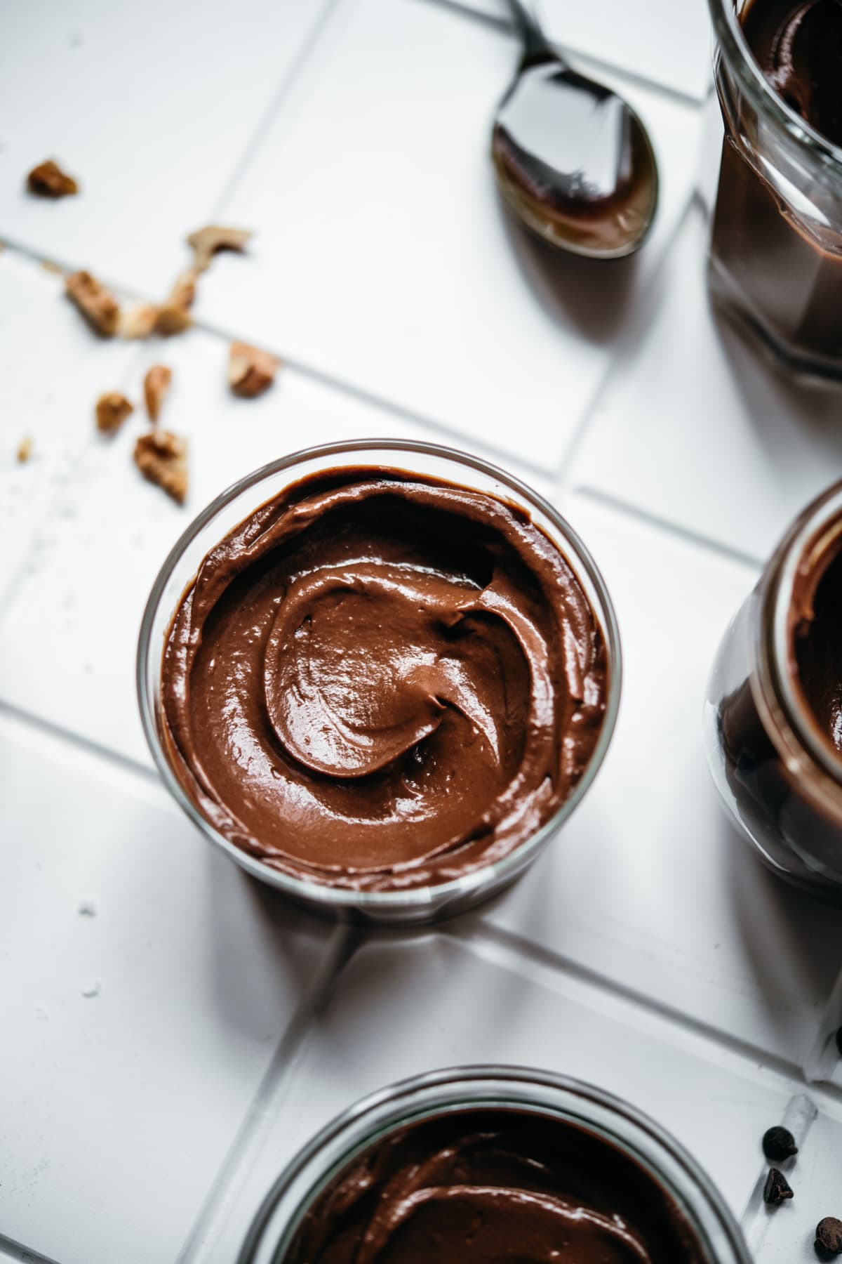 overhead view of jars of vegan avocado chocolate mousse on white tile. 