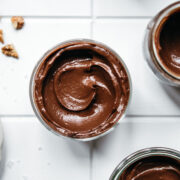 overhead view of jars of vegan avocado chocolate mousse on white tile.