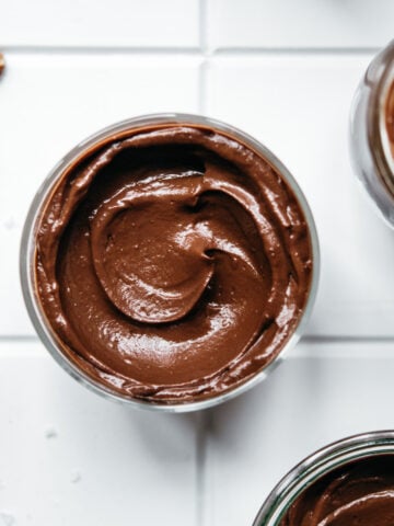 overhead view of jars of vegan avocado chocolate mousse on white tile.