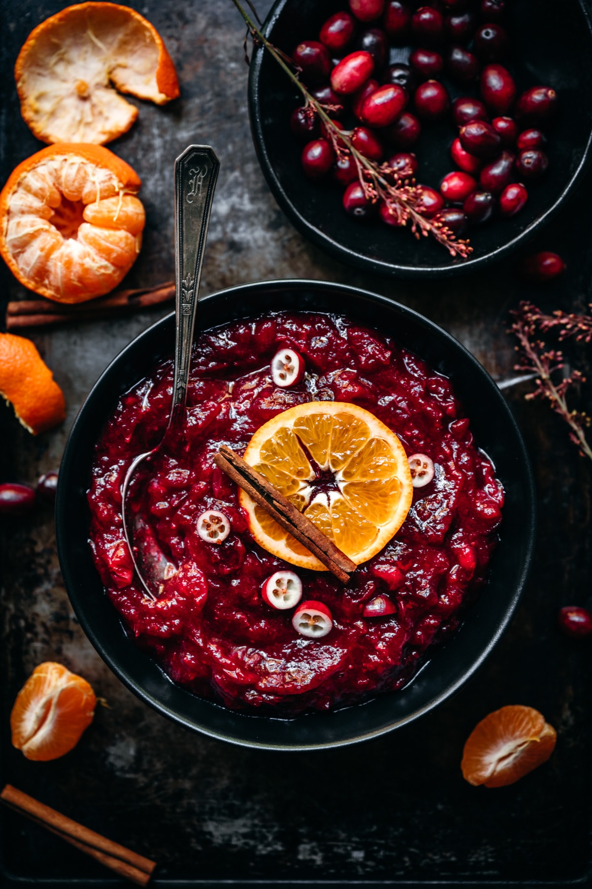 overhead view of cranberry sauce in a black bowl garnished with orange slice and cinnamon stick.