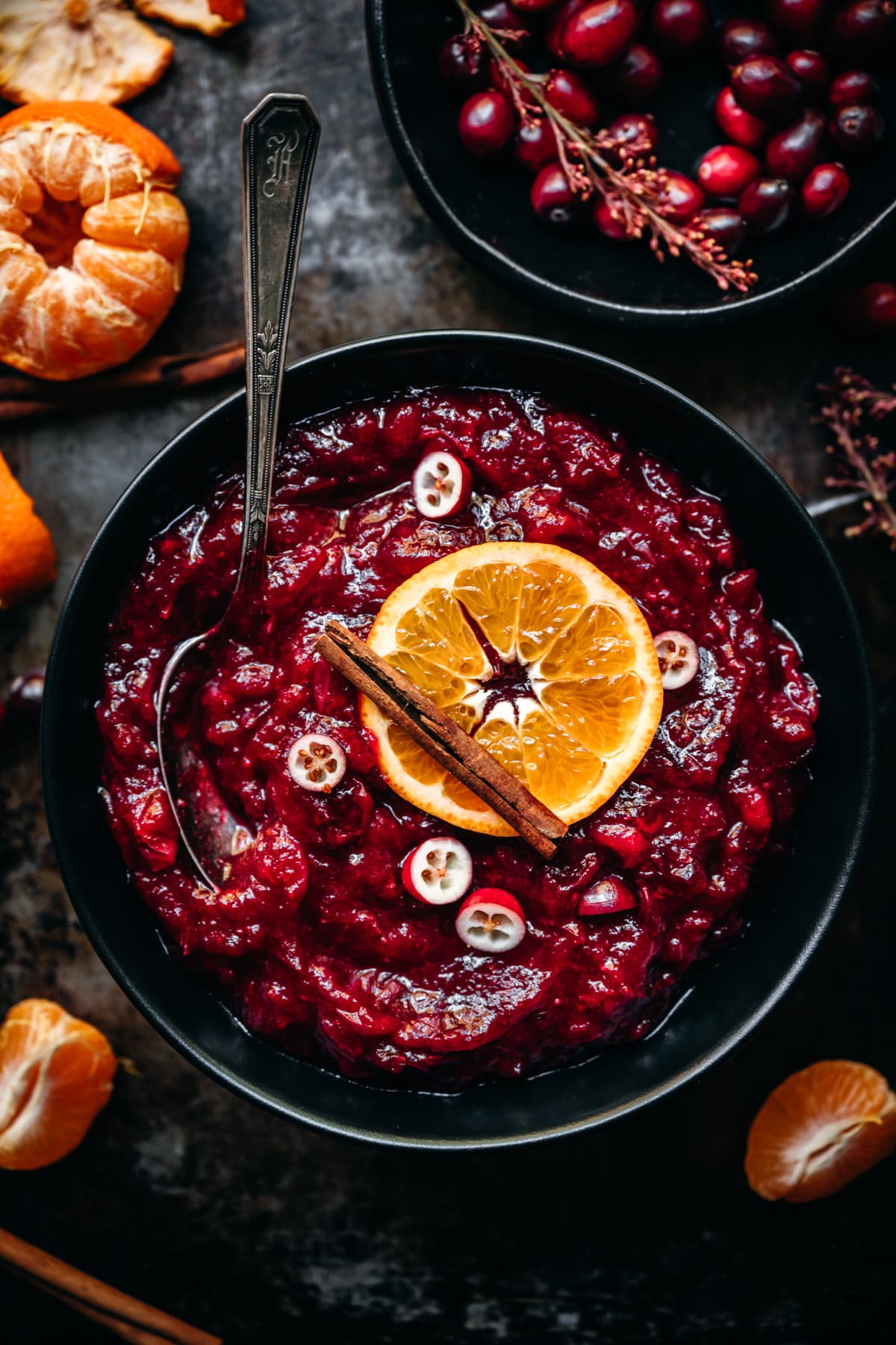 overhead view of cranberry sauce in a black bowl garnished with orange slice and cinnamon stick.