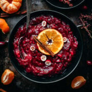 overhead view of cranberry sauce in a black bowl garnished with orange slice and cinnamon stick.