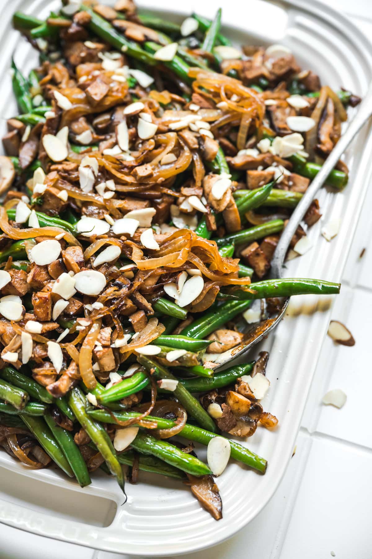 close up side view of vegan green beans with tofu bacon, mushrooms and caramelized onions on white platter.