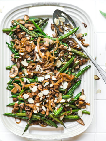 overhead view of vegan green beans with tofu bacon, mushrooms and caramelized onions on white platter.