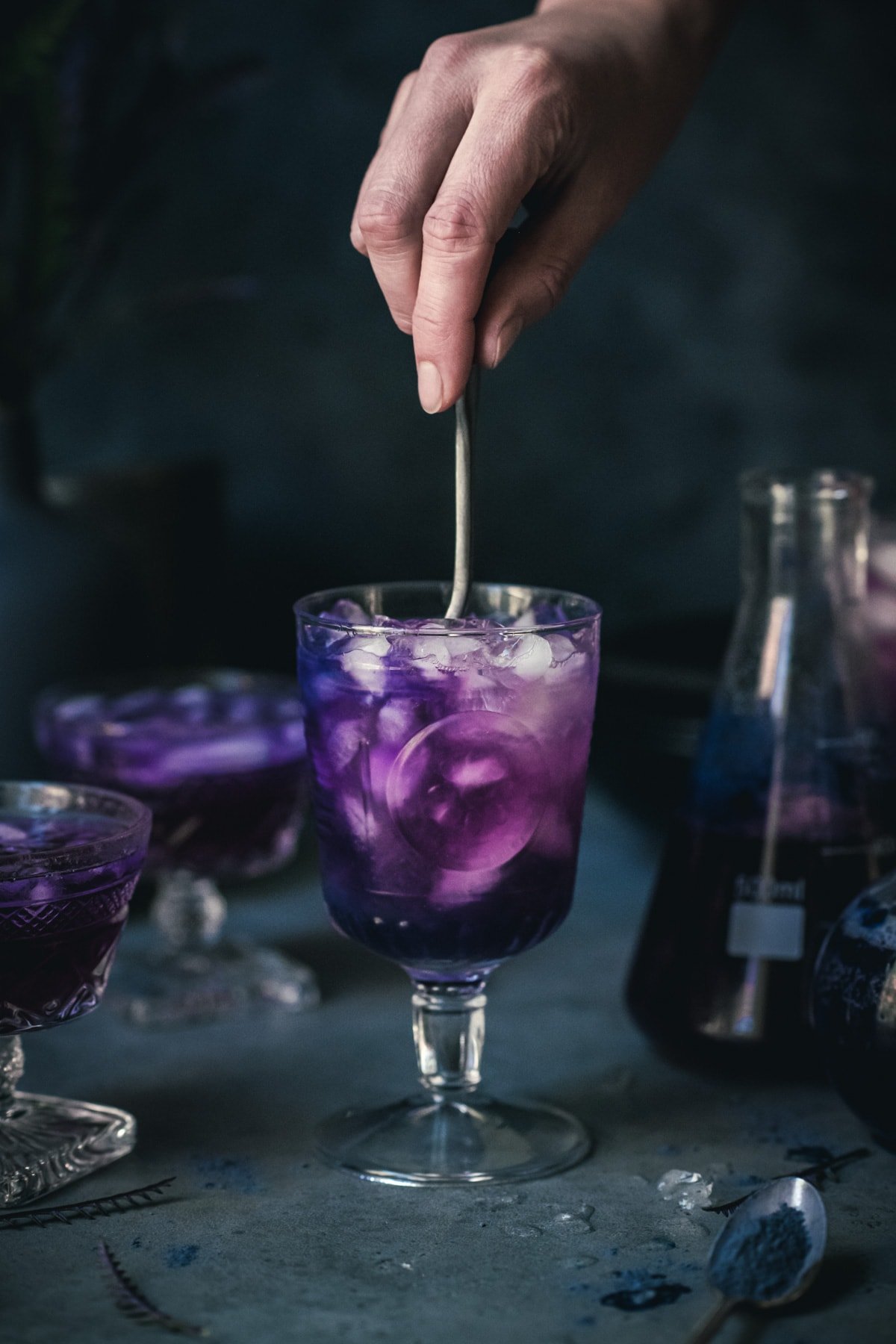 person stirring a purple halloween cocktail in a goblet glass.