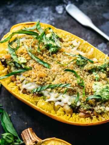 close up side view of spaghetti squash filled with pesto, white beans and topped with breadcrumbs.
