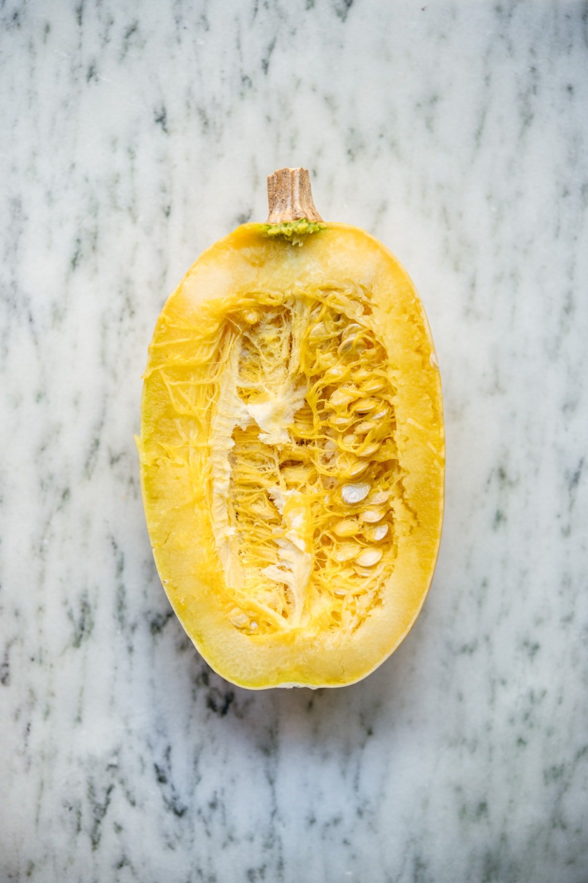 overhead view of spaghetti squash sliced in half on marble surface.