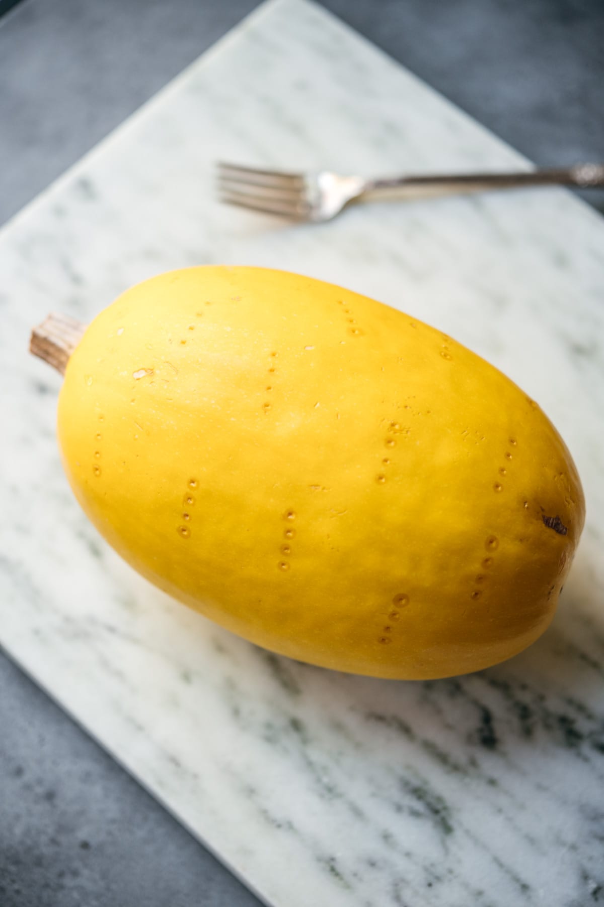 close up side view of whole spaghetti squash with fork marks. 