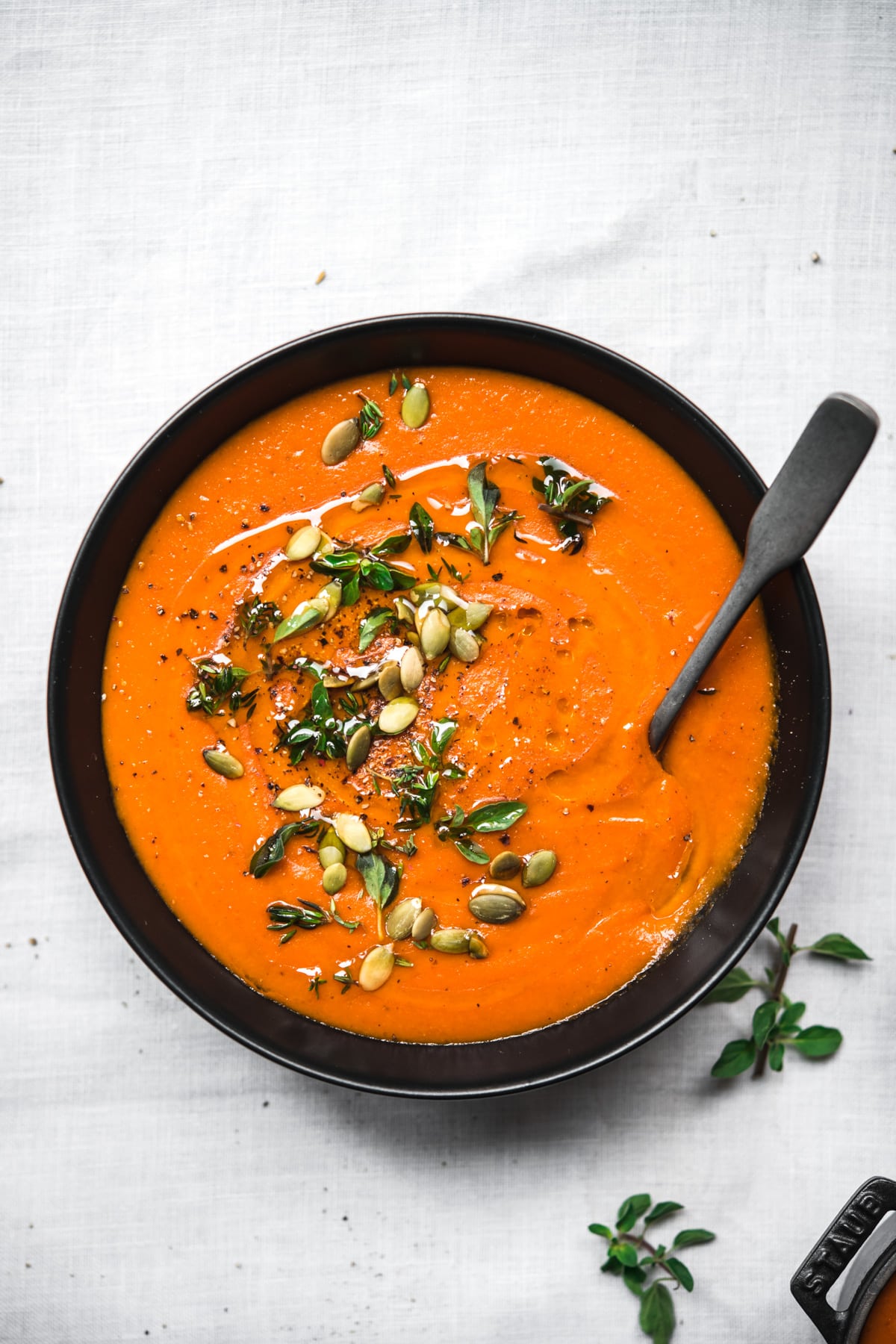 overhead view of bowl of vegan roasted red pepper soup on white tablecloth.