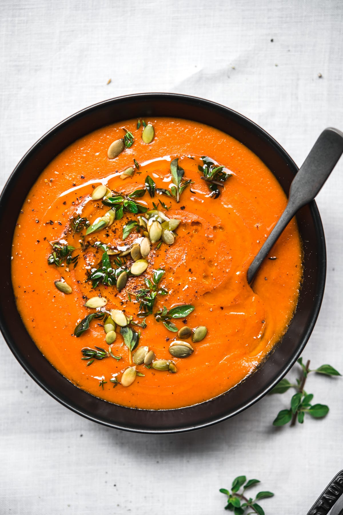 overhead view of bowl of vegan roasted red pepper soup on white tablecloth.