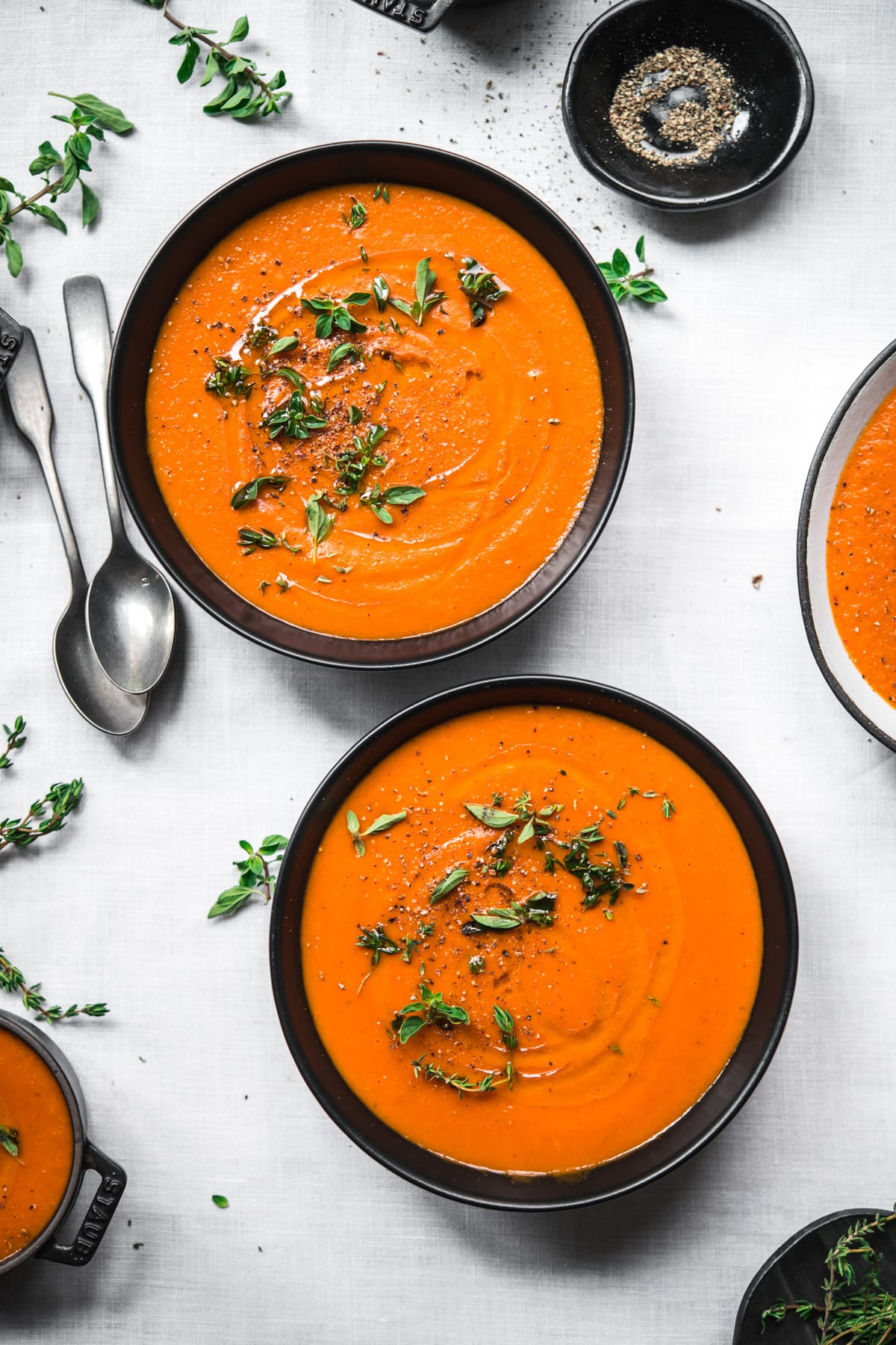 overhead view of two bowls of roasted red pepper soup garnished with olive oil and fresh herbs.