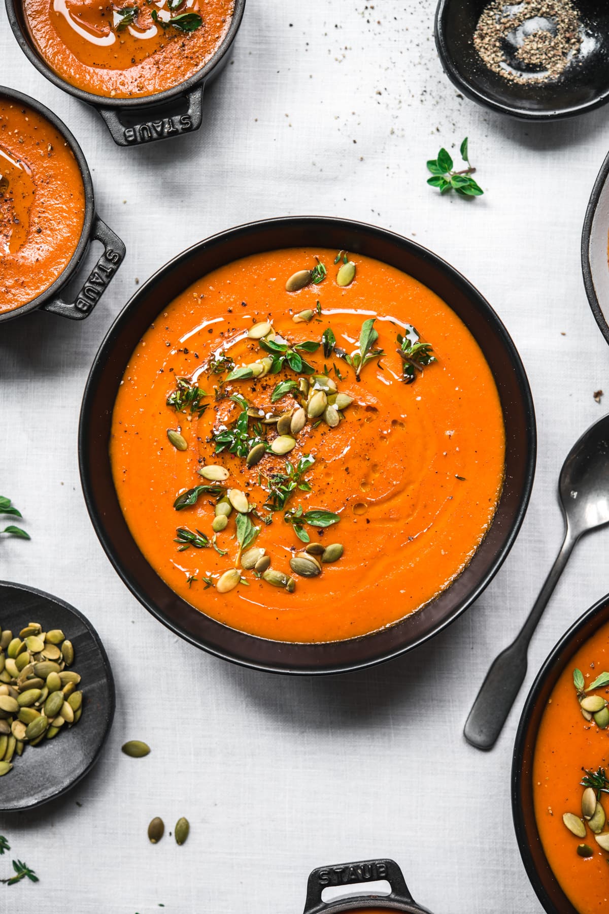 overhead view of bowl of vegan roasted red pepper soup on white tablecloth.