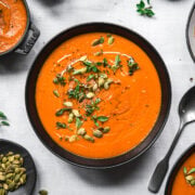overhead view of bowl of vegan roasted red pepper soup on white tablecloth.