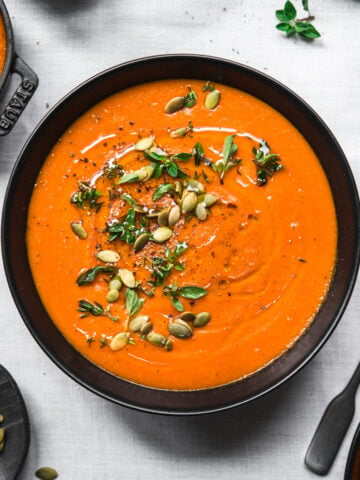 overhead view of bowl of vegan roasted red pepper soup on white tablecloth.