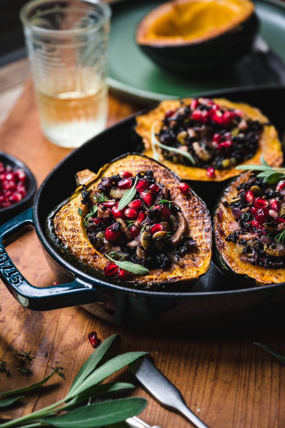 side view of vegan stuffed acorn squash with black rice, mushrooms and pomegranate seeds on top.
