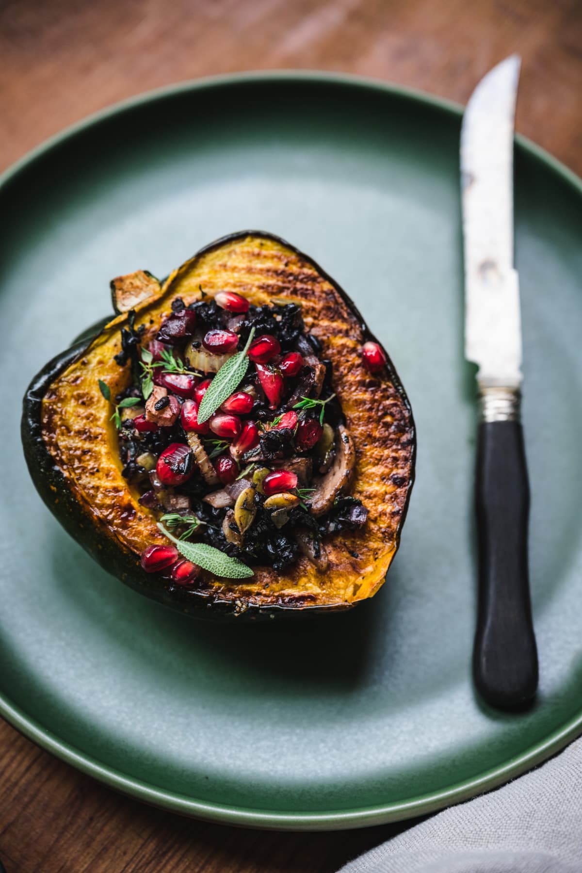 side view of vegan stuffed acorn squash with black rice, mushrooms and pomegranate seeds on top.