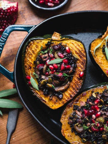 overhead view of slices of vegan stuffed acorn squash with black rice, mushrooms and pomegranate seeds on top.