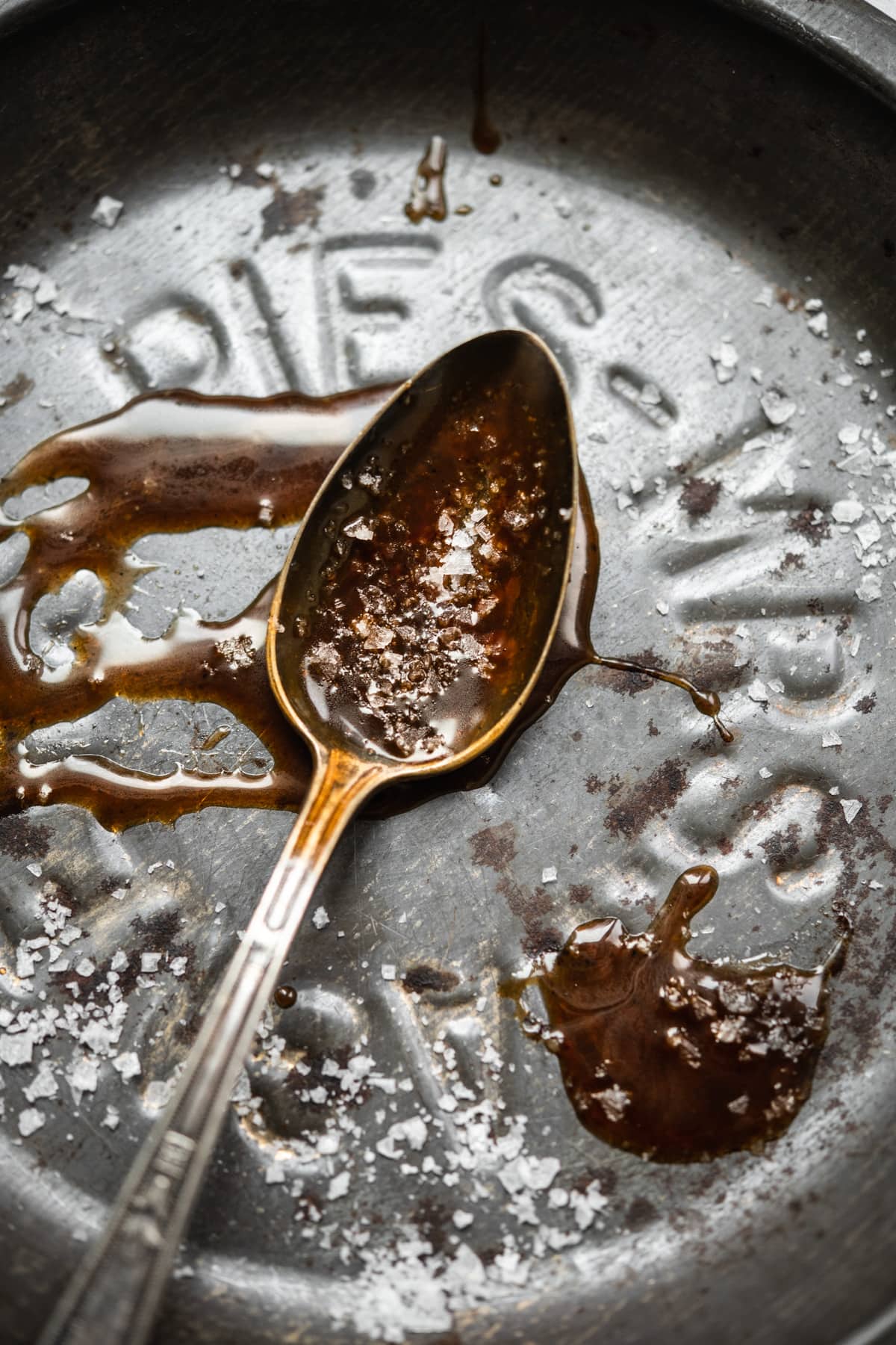 close up view of vegan salted caramel on an antique spoon with flaky salt on top.