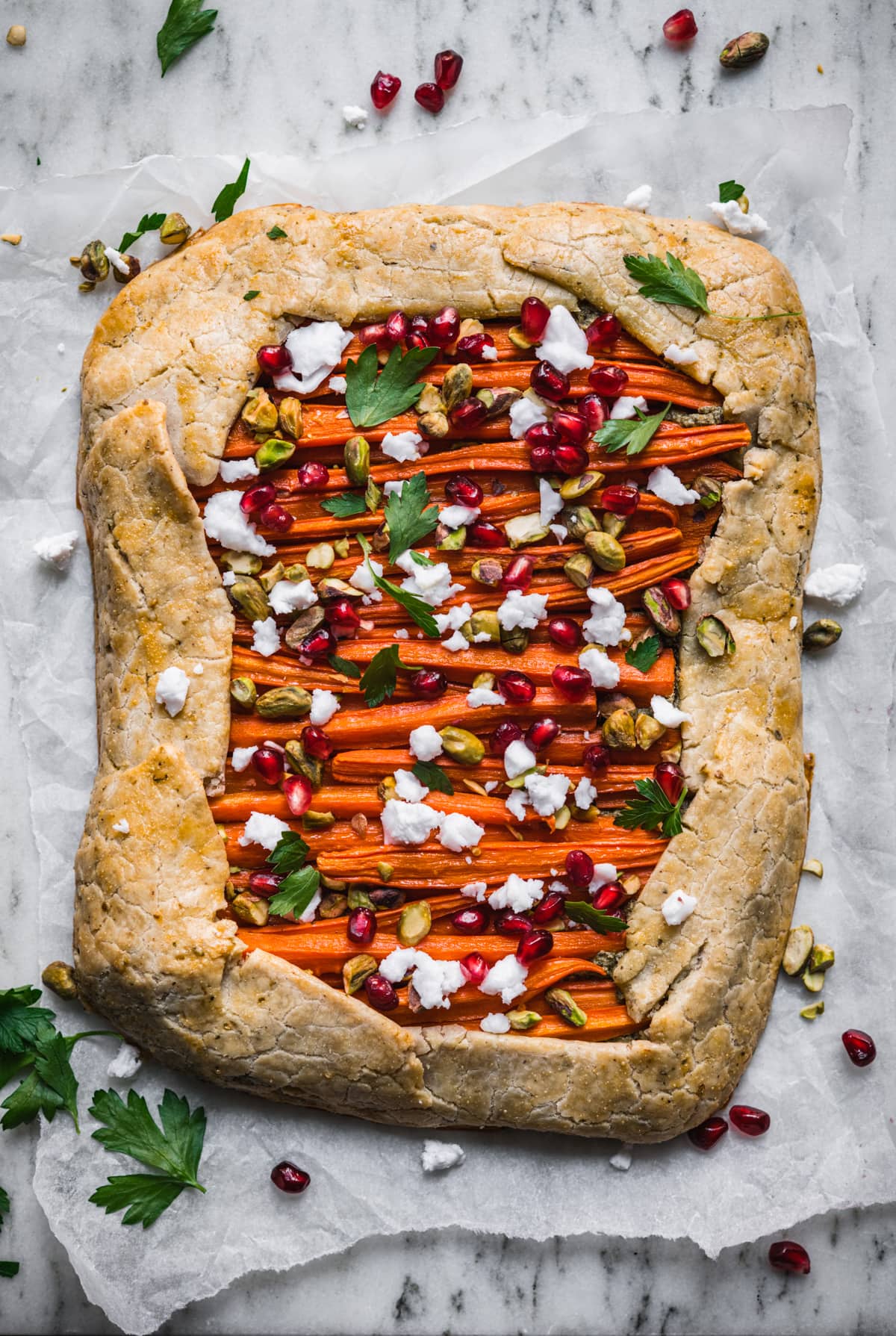 overhead view of vegan and gluten free carrot tart with pomegranate, pesto and pistachios.