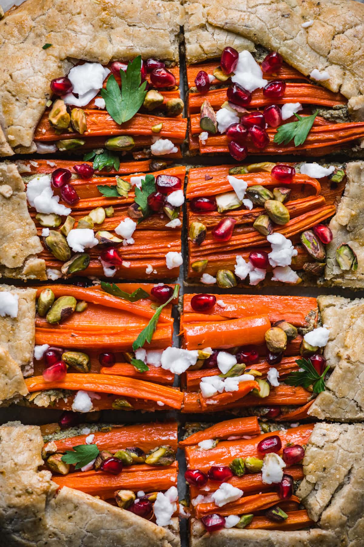 overhead view of sliced carrot tart with pomegranate, pesto and pistachios.
