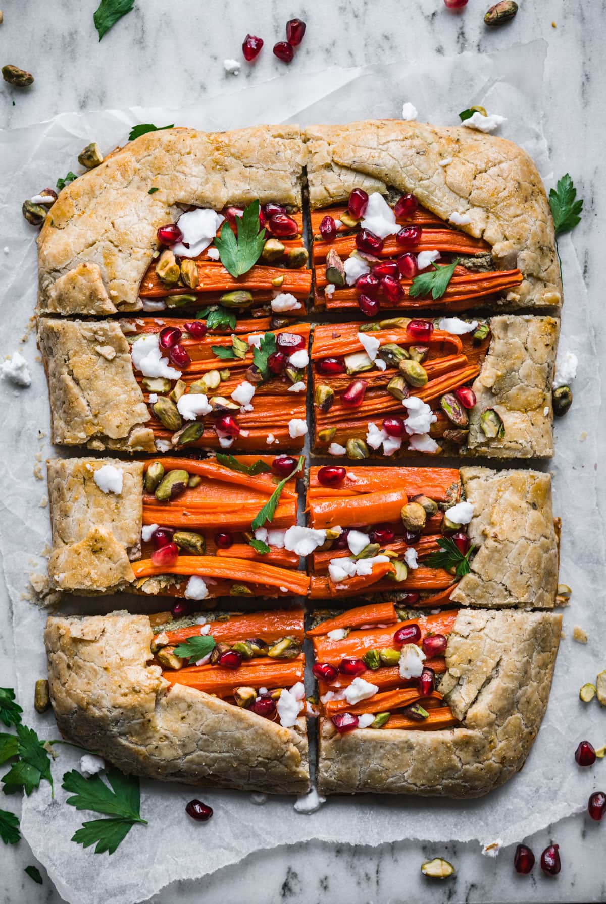 overhead view of sliced carrot tart with pomegranate, pesto and pistachios.