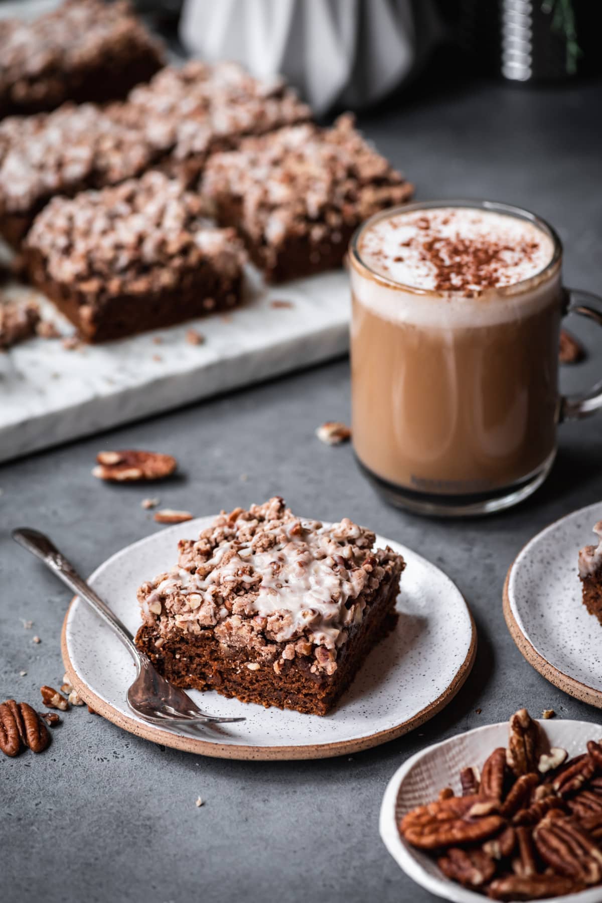 close up view of vegan gingerbread coffee cake slice on a small ceramic plate with latte in background. 