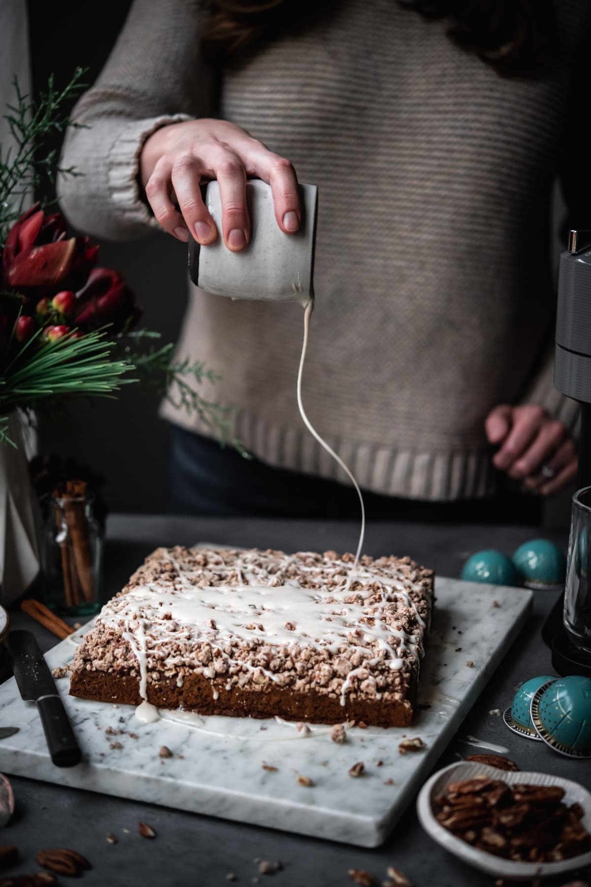 person drizzling vanilla glaze onto coffee cake. 