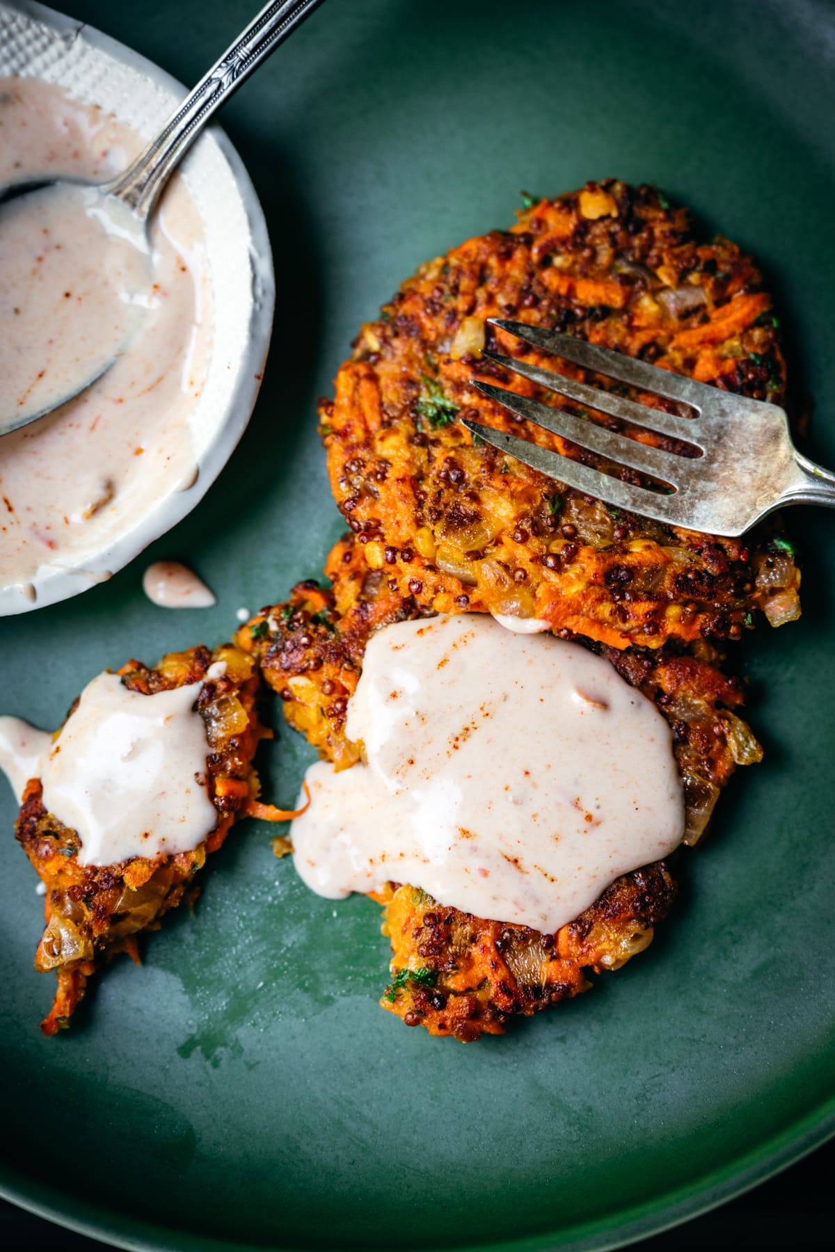 close up view of two vegan carrot fritters on a plate with harissa yogurt sauce.