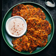 close up overhead view of vegan carrot fritters on a green plate with harissa yogurt sauce on the side.