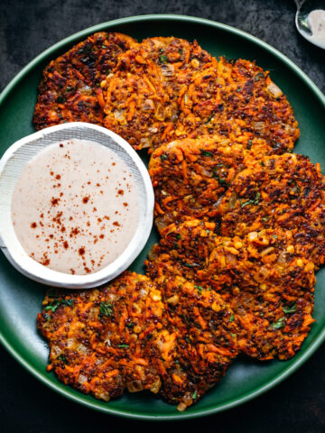 close up overhead view of vegan carrot fritters on a green plate with harissa yogurt sauce on the side.