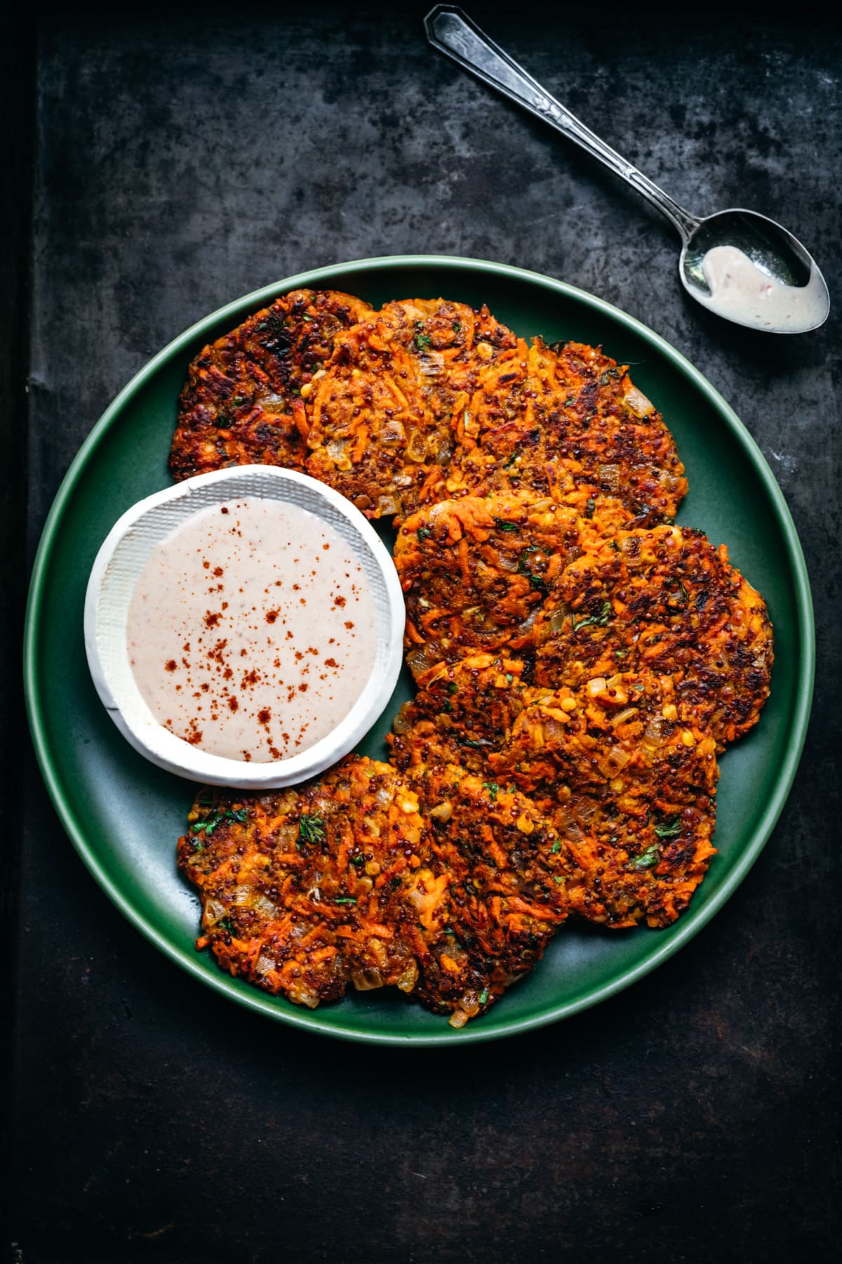 close up overhead view of vegan carrot fritters on a green plate with harissa yogurt sauce on the side.