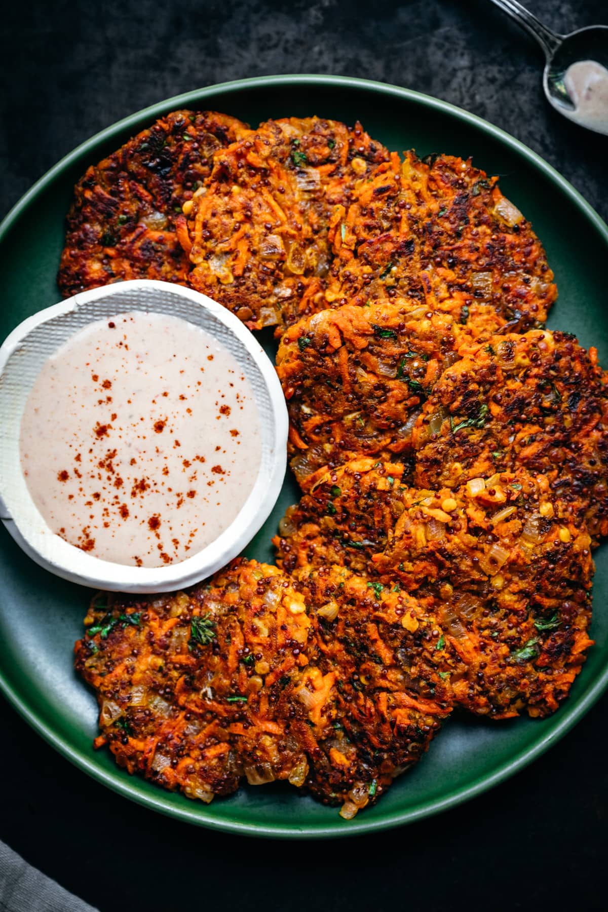 close up overhead view of vegan carrot fritters on a green plate with harissa yogurt sauce on the side.