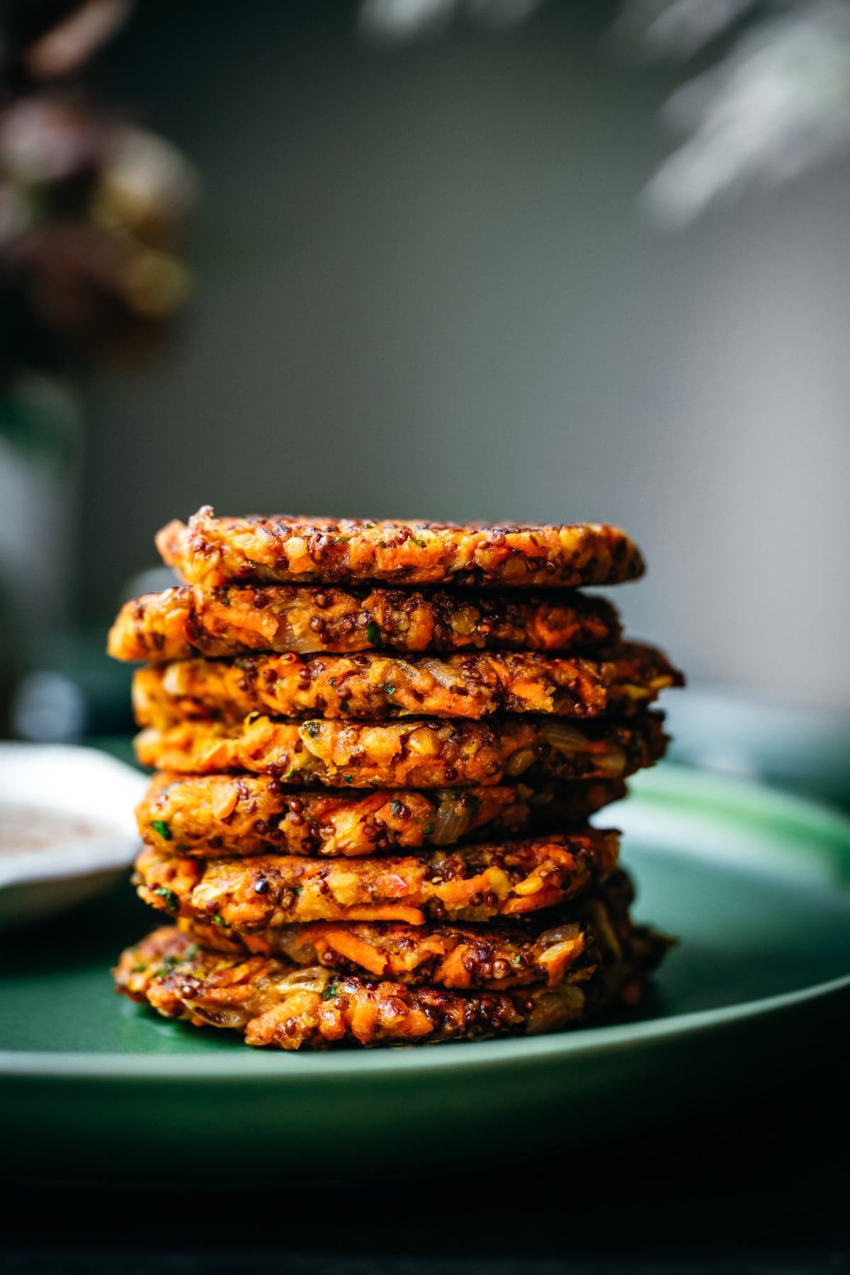 close up side view of a stack of carrot fritters on a green plate.