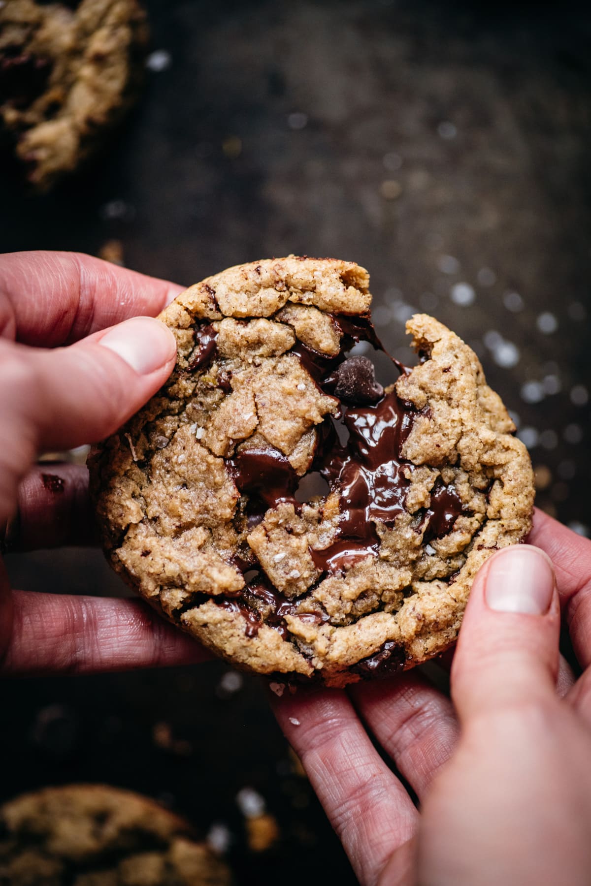 close up view of two hands pulling apart a freshly baked chocolate chip cookie. 