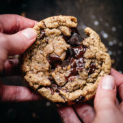 close up view of two hands pulling apart a freshly baked chocolate chip cookie.