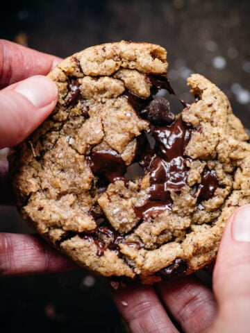 close up view of two hands pulling apart a freshly baked chocolate chip cookie.