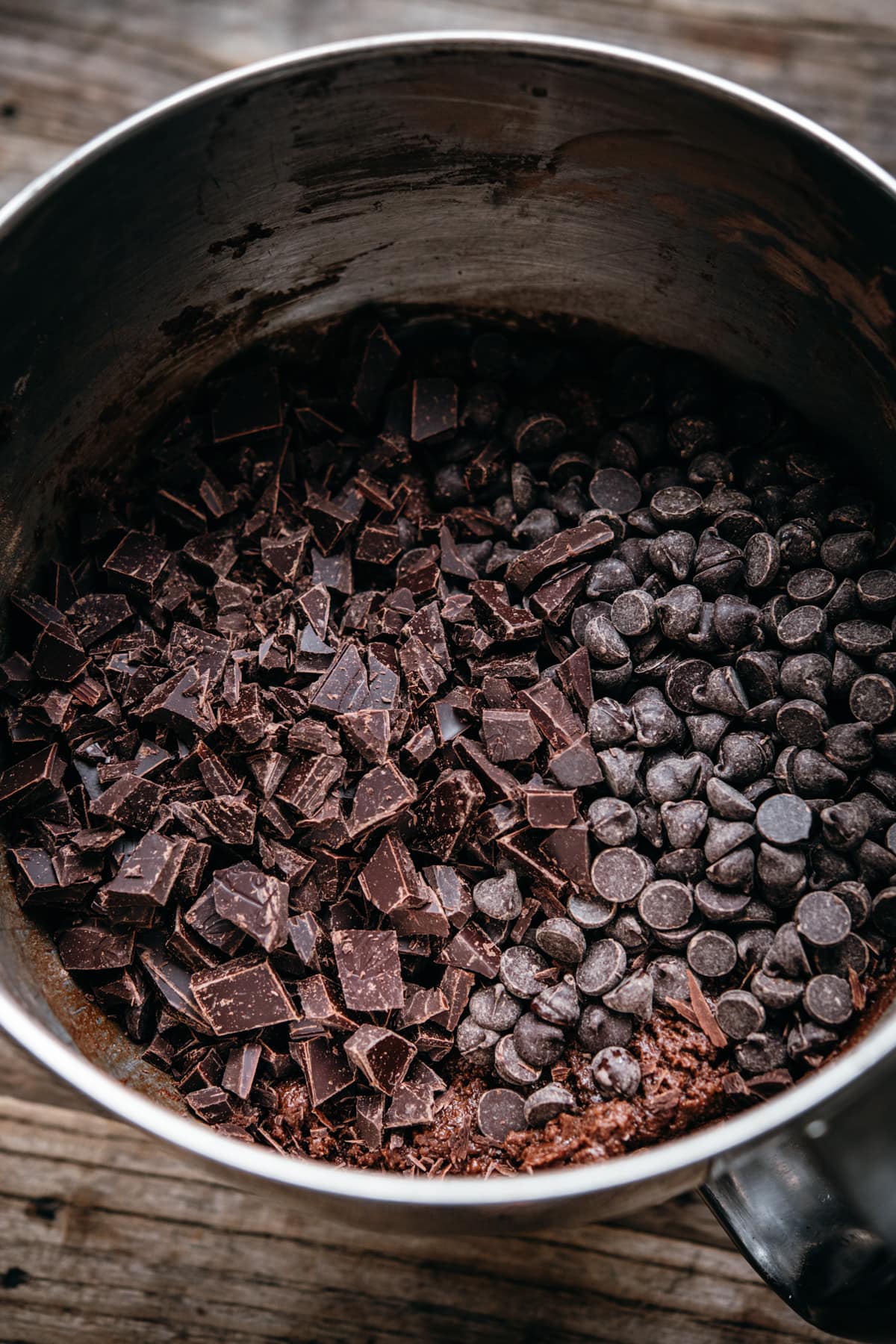 close up view of chocolate cookie dough in mixing bowl with two types of chocolate.