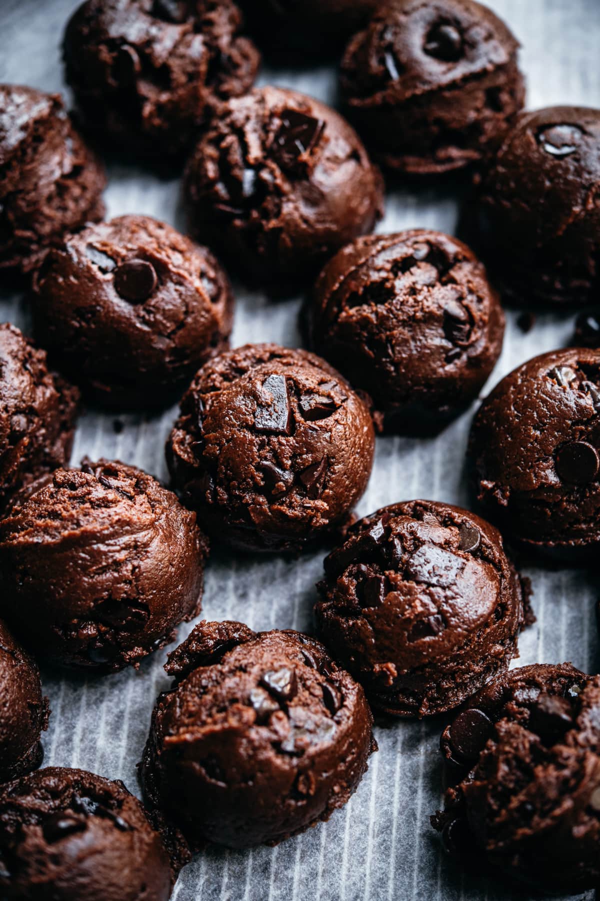 side view of chocolate cookie dough balls on parchment paper. 