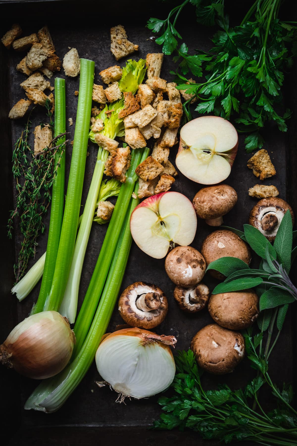 overhead view of ingredients for stuffing on a baking sheet, including celery, apple, mushrooms, onions and toasted bread. 