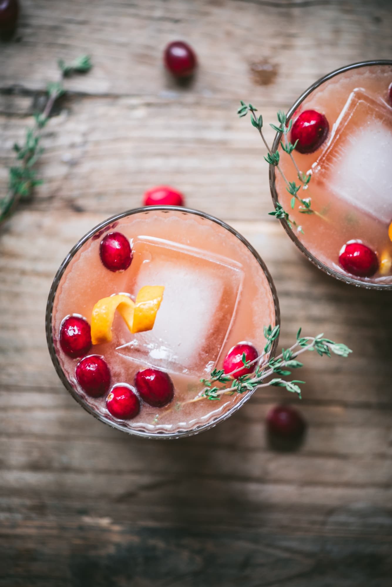 Close up of cranberry orange cocktails garnished with fresh thyme.